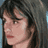 Pixelated static image of a person's face with dark hair and light skin, cropped to show profile from shoulders up against a gray background.
