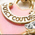 A circular pink icon with gold and white text reading "MONEY COUTURE" and a silver and gold emblem on a pink background.