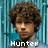Pixelated portrait of a person with curly brown hair against a blue striped background, with text labels and symbols overlaid.