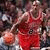 Pixelated static image of a basketball player in mid-action wearing red jersey and dark shorts, holding an orange basketball with visible fingers.