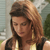 A pixelated close-up of a person with light brown hair wearing a black and gold sleeveless top against a blurred outdoor background.
