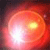 A circular pixelated image with a bright white center transitioning to orange and red hues, featuring two distinct light sources on the right side.