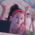 Pixelated image of a person with dark hair tied back, wearing a pink headband and dark clothing, holding a white object near their face.