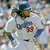 A baseball player in a white uniform with blue and red accents holds a bat, wearing a helmet and yellow face mask.