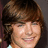 Pixelated close-up of a person with brown hair and a light-colored top against a dark background.