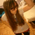 A pixelated image of a person with long brown hair wearing a white top and dark pants, standing in front of a blurred background.