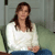 A pixelated image of a person with long brown hair wearing a white top and blue pants, seated against a muted green and gray background.