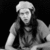 Black-and-white animated icon shows a person with long dark hair wearing a light-colored head covering and dark shirt, seated against a black background.