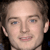 Pixelated close-up of a person's face with light skin, blue eyes, and brown hair, showing a neutral expression with lips slightly parted.