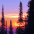 Pixelated sunset scene with multiple dark spires against a gradient sky transitioning from purple to orange, featuring a bright sunburst near the horizon.