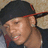 Pixelated close-up of a person wearing a dark cap with red trim, light brown skin tone, and visible ear.