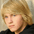 A pixelated image of a person with light brown hair and blue eyes, wearing a black top against a beige background.
