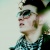Pixelated static image of a person's face in profile with dark hair and sunglasses, wearing a checkered shirt against a light background.
