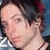 Pixelated close-up of a person with short dark hair, light skin, and a neutral expression, wearing a dark top with a light collar and a thin dark necklace.