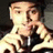 Pixelated static image of a person with light skin tone wearing dark clothing and holding an object near their face.
