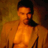 Static pixelated image of a shirtless person with dark hair against warm-toned background, rendered in orange-yellow color palette with low-resolution dithering and visible compression artifacts.