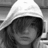 Black-and-white image of a hooded figure with obscured face alongside red pixelated text on black background.