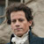 Pixelated portrait of a person with dark curly hair wearing a white shirt and dark jacket against a blurred background.
