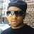 Pixelated portrait of a person wearing dark sunglasses and a dark cap, with light skin tone and visible facial features against a blurred background.