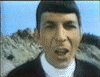 A man in a dark jacket and white shirt appears in showing facial expressions and head movements against a rocky background