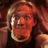 Pixelated static image of a person with light brown hair and orange-toned skin wearing a dark top against a blurred background.