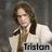 A person with long brown hair wears a white jacket over a brown shirt, positioned against a gray background with the name 'Tristan' displayed below.