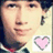 Pixelated close-up of a person's face with dark hair, wearing a checkered shirt and red tie, featuring a pink heart symbol in the bottom right corner.