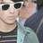 Pixelated close-up of a person wearing white-framed sunglasses and light blue clothing, with dark hair visible on the right side.