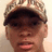Pixelated close-up of a person wearing a camouflage cap with dark brim, light brown skin tone, and visible facial features including eyes, nose, mouth, and ear.