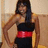 A pixelated figure with long dark hair wears a black top and red belt, standing against a light brown background.