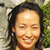 A static pixelated portrait of a person with long dark hair, closed eyes, and a smiling expression against a blurred background of green and beige tones.