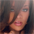 Pixelated close-up of a person with light skin tone, dark hair, and pink lips, wearing a dark top against a blurred background.
