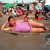 A pixelated static image shows a person lying on a light brown surface, wearing a pink sleeveless top, with a blurred background of green and brown tones.