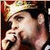 Pixelated static image of a person's face with hand near mouth, wearing dark cap and light-colored shirt against dark background.