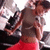A person in a gray crop top and red shorts stands with arms crossed, head tilted down, against a blurred background with dark and light shapes.