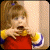 Pixelated static image of a cartoon character with brown hair wearing a red dress and yellow sleeves, holding an object near their mouth against a light background.