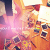 A static image shows a wooden floor with scattered items including polaroid-style photos, a colorful patterned rug, and a pinkish light effect with partially visible text.