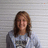 Pixelated static image of a person with long brown hair wearing a light blue shirt against a striped background.