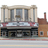 Static pixelated image of a building facade with columns, a red and white striped awning, and a brown brick section with a chimney.