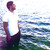 Pixelated image of a figure in white shirt and dark pants standing on a wooden structure near water with a blurred background.