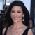 Pixelated image of a person with long dark hair wearing a black strap top, smiling with eyes closed against a blurred background.