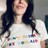 A pixelated image of a person with long dark hair wearing a white top with colorful patterns, seated against a neutral background.