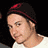Pixelated static image of a person wearing a dark beanie with red accents and a white shirt against a black background.