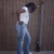 Pixelated figure in white top and blue pants holding dark object near face against brown background.