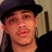 Pixelated close-up of a person wearing a dark flat cap, light-colored shirt, and dark jacket against a neutral background.