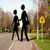 Two black silhouettes stand on a path with autumn trees and a yellow sun symbol in the background.