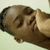A person with short dark hair and light skin rests their hand on their chin, smiling slightly against a pale background.