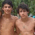 Two shirtless individuals with dark hair stand side-by-side against a blurred green background with hints of blue and brown.