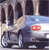 Pixelated image of a light blue car with red taillights, positioned on a road with dark vertical shapes in the background.