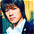 Static pixelated image of a person with dark hair wearing a white shirt and dark jacket against a colorful background.